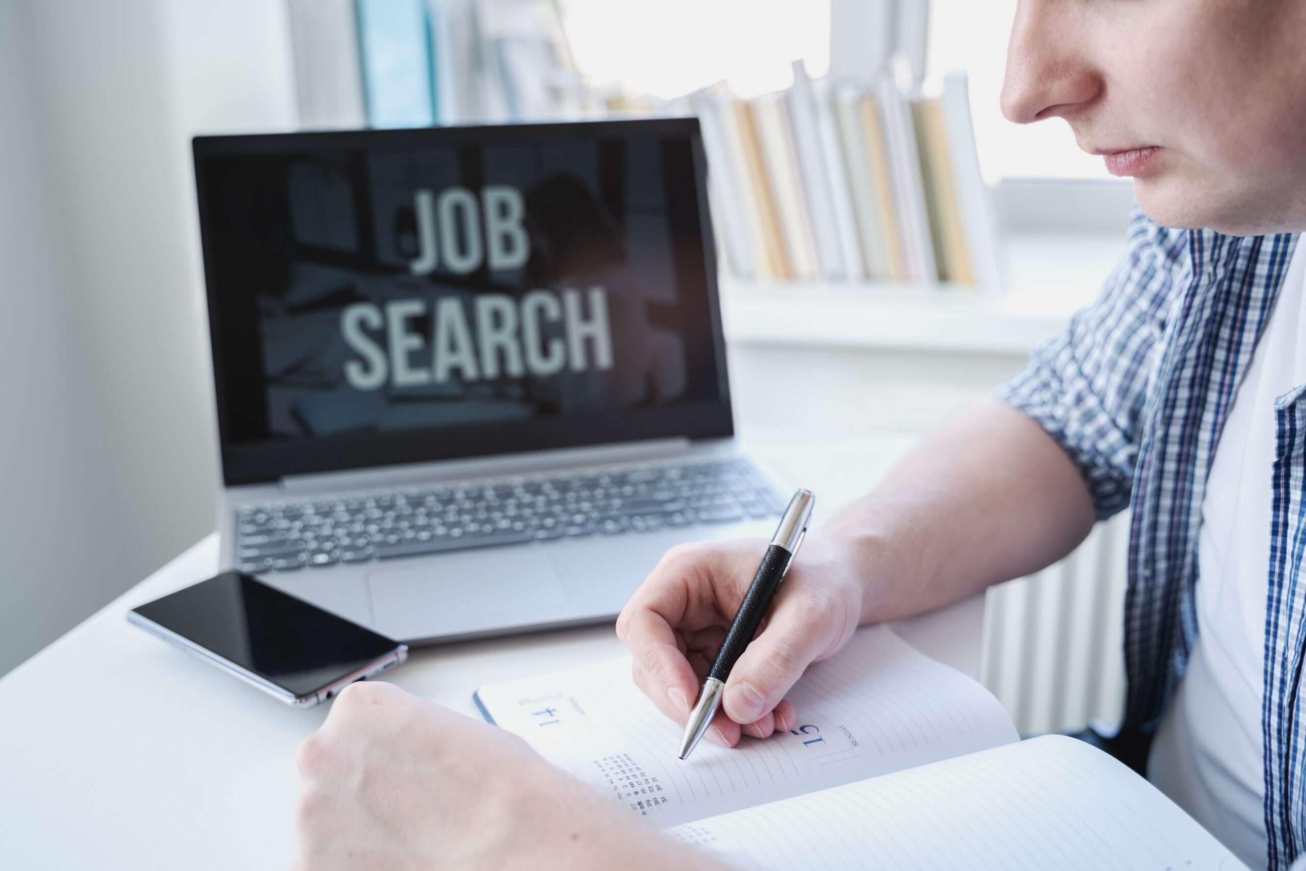A male writing in his notebook while doing job search.